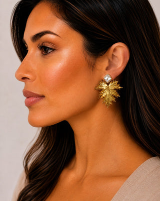 Woman wearing gilded palm leaf earrings with faux pearl detail