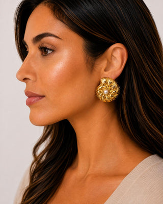 Woman wearing gold-tone spiral seashell stud earrings with faux pearl center